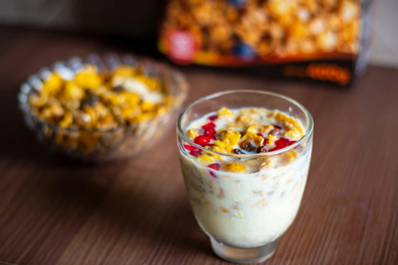 a dessert sits in a glass next to a bowl of cereal