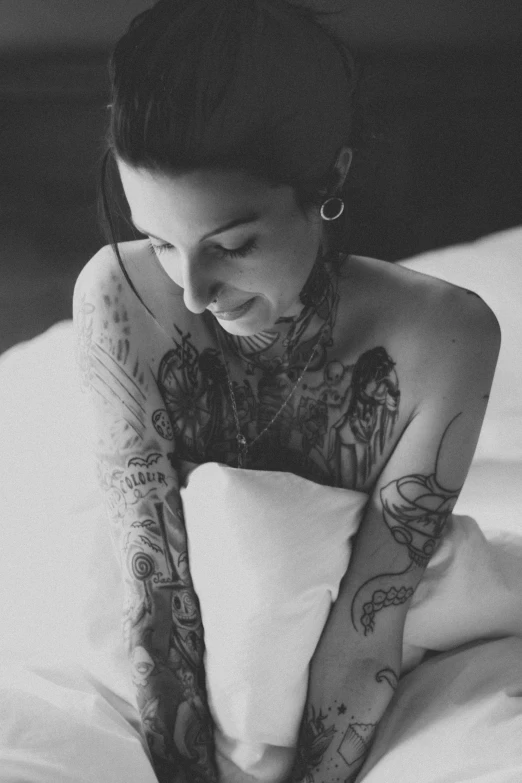 woman with tattoo on stomach laying in bed holding pillow