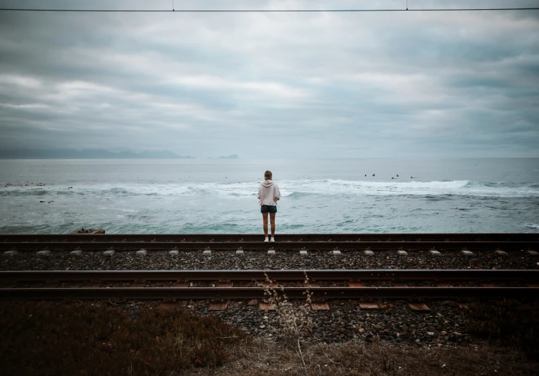 a person standing on a train track next to the water