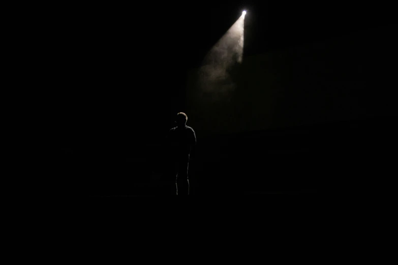 the person in the dark with their arm outstretched is silhouetted by a spotlight