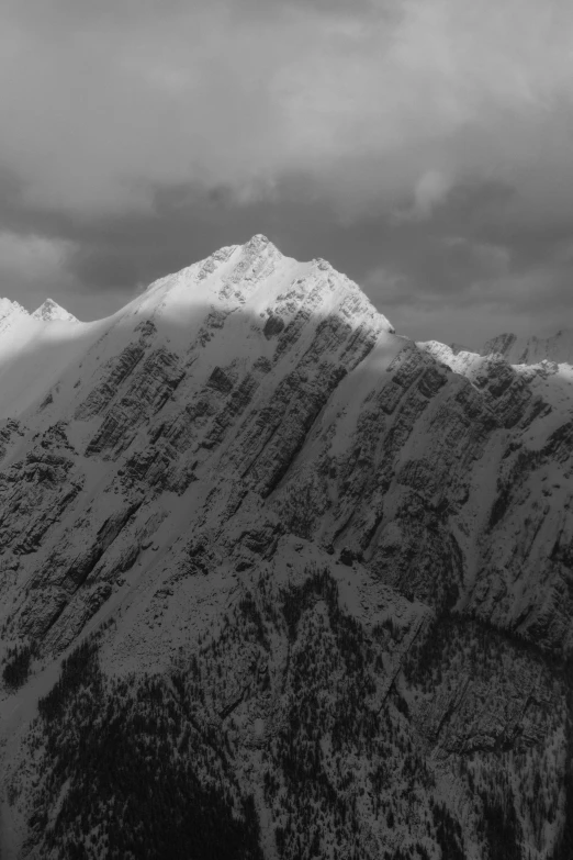 black and white image of mountains, clouds, trees and snow