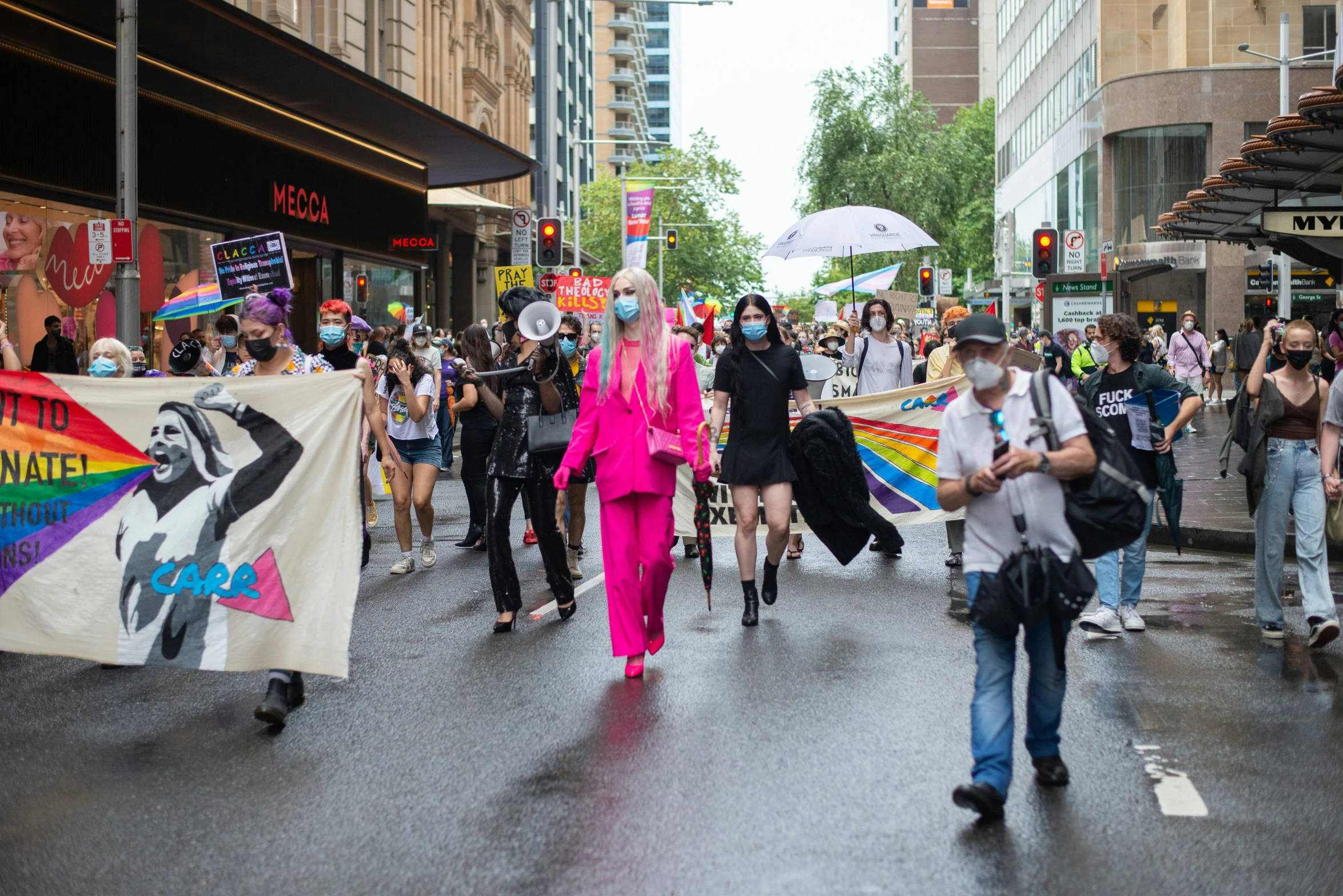 a street parade with several people wearing mask and carrying signs and banners