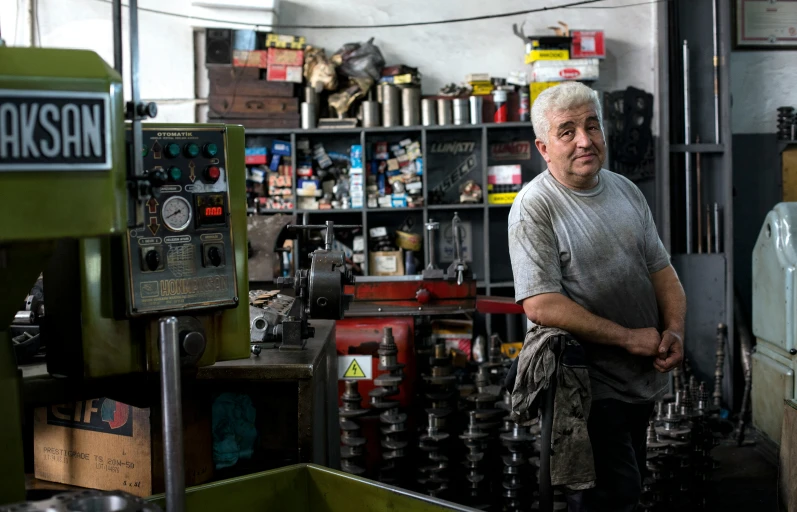 an old man standing in his workshop with a rack full of machinery