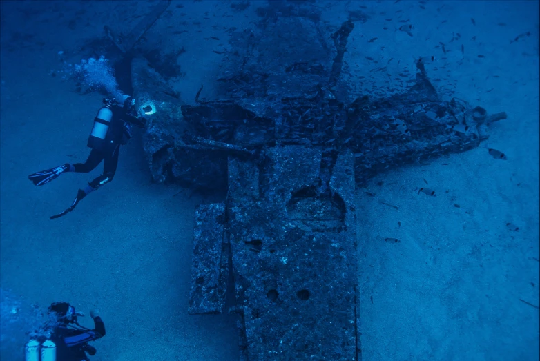 two scubas swim next to an old sunken ship