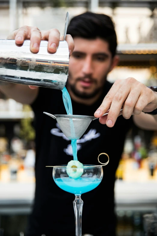 the bartender is pouring a blue drink into a martini glass