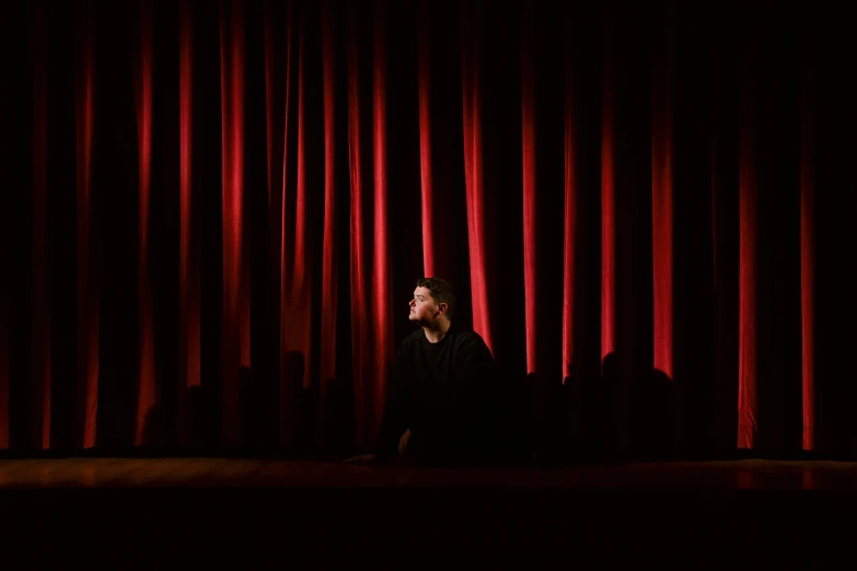 a woman sitting in front of a red curtain