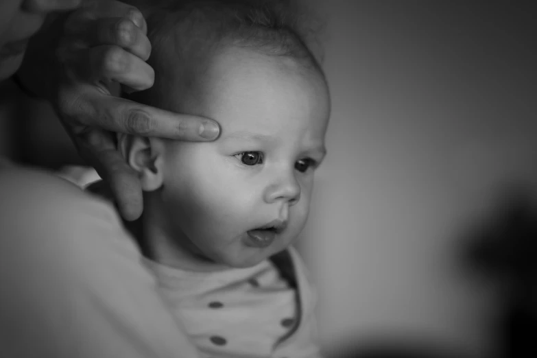 a baby holding his head near an adult's hand