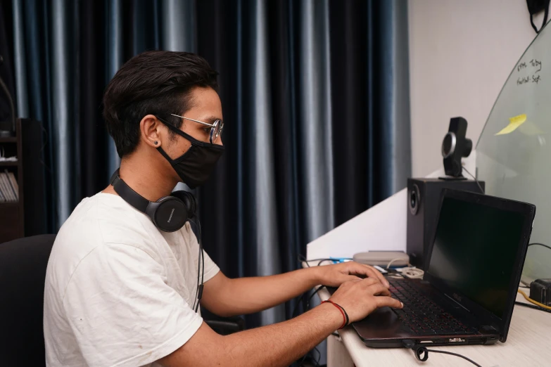 a man wearing a black mask typing on his laptop