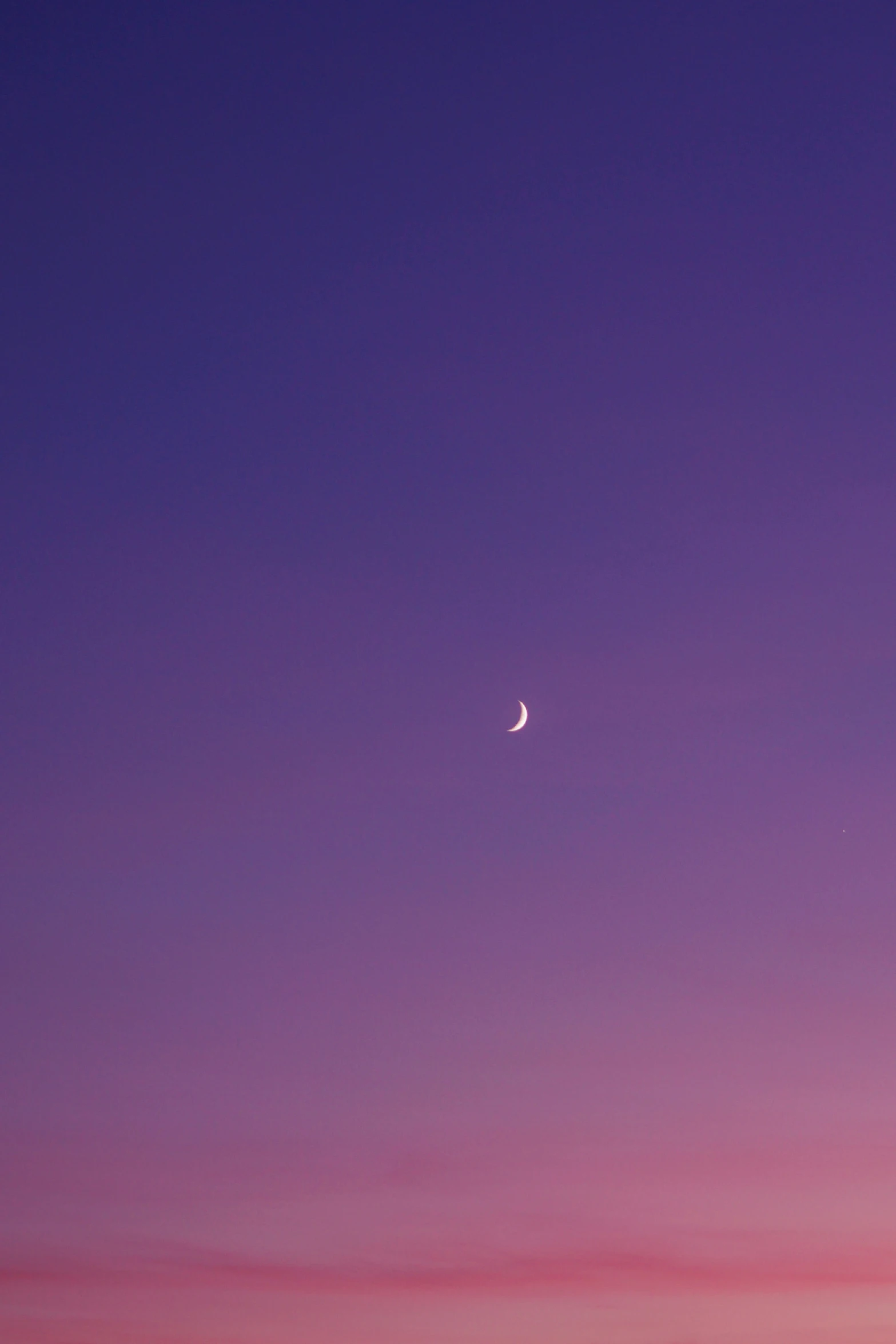 a distant crescent moon in the dark sky