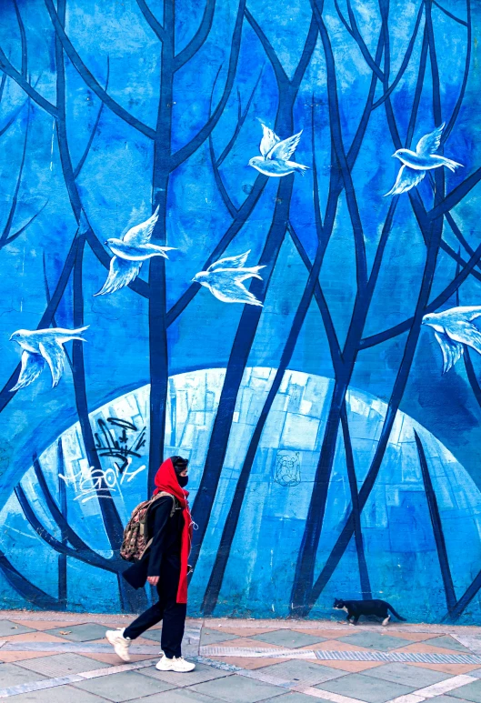 a person walking in front of a blue wall with trees and animals painted on it