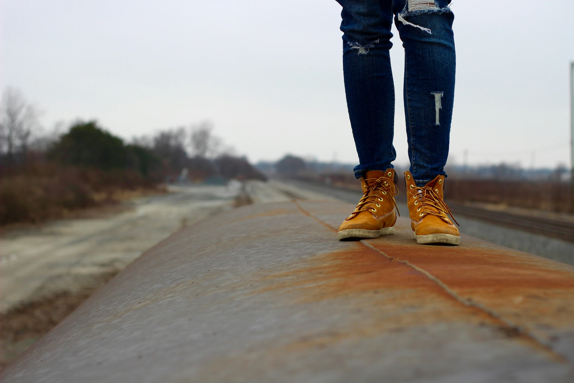 person's legs standing on railroad track during the day