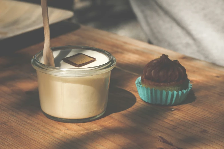 a glass with a wooden spoon and some food on the table