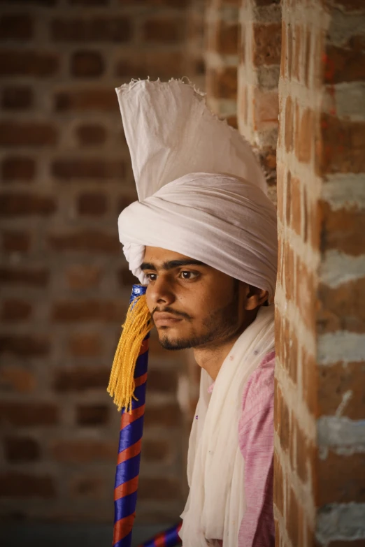 a man with a very colorful head piece, posing against a brick wall