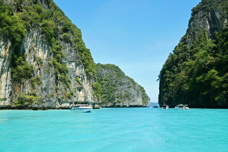 small boats floating near the shoreline and cliffs