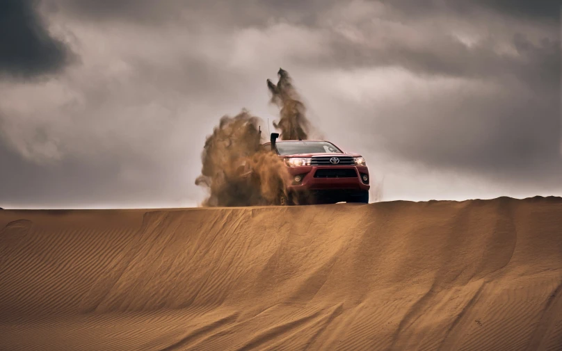 a red four door car kicking up dirt on sand dunes