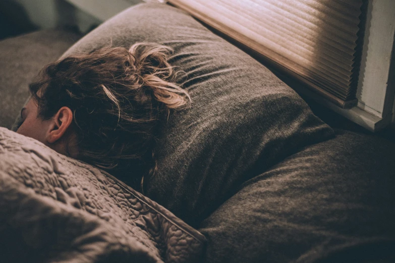 a woman laying on top of a brown couch under a window