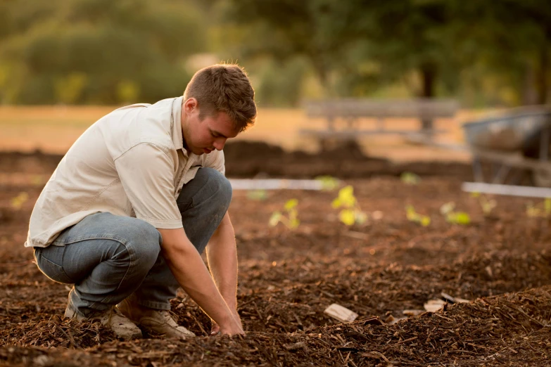 man kneels in his muddy field to place a handful of seed