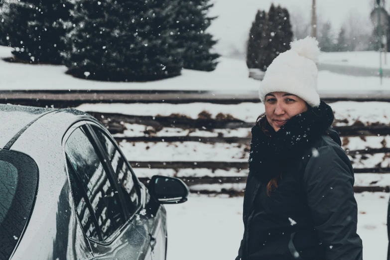 a woman wearing a white beanie and looking into the distance as snow begins to fall