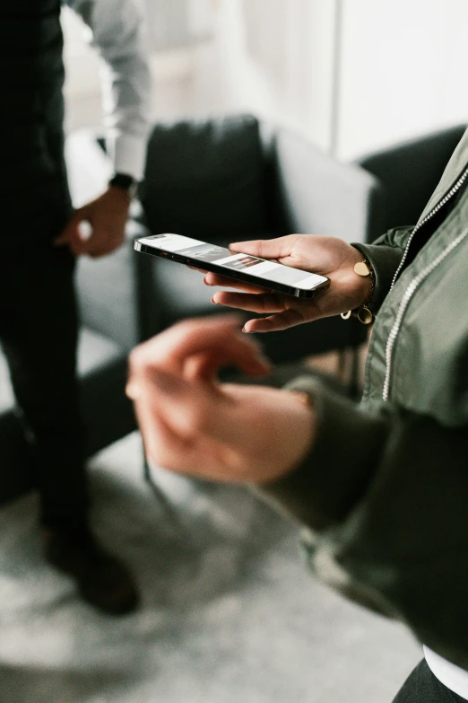 person in green jacket holding a cellphone on a small white table