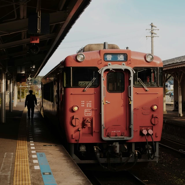 a train pulls up to a platform while a lone man stands nearby