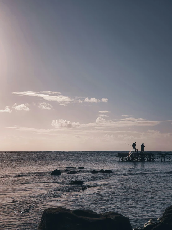 two people stand on a pier next to the water