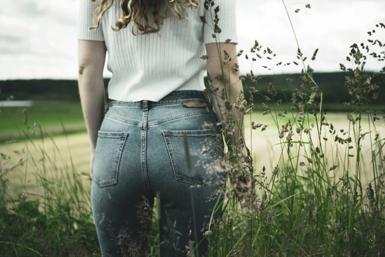 a person wearing jean pants stands in tall grass