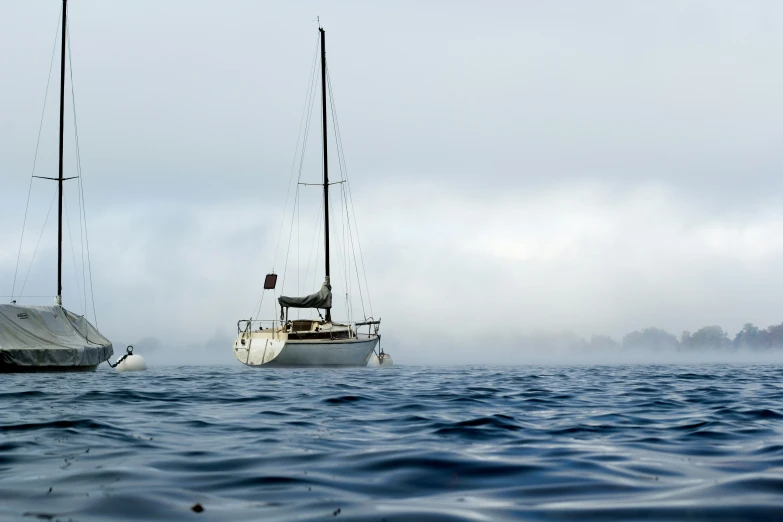 two sailboats float close together in the fog