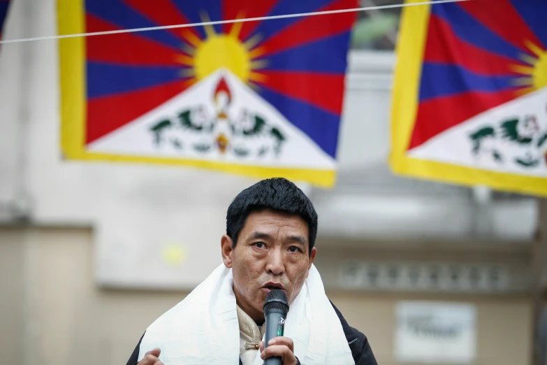 a man speaking into a microphone with flags in the background