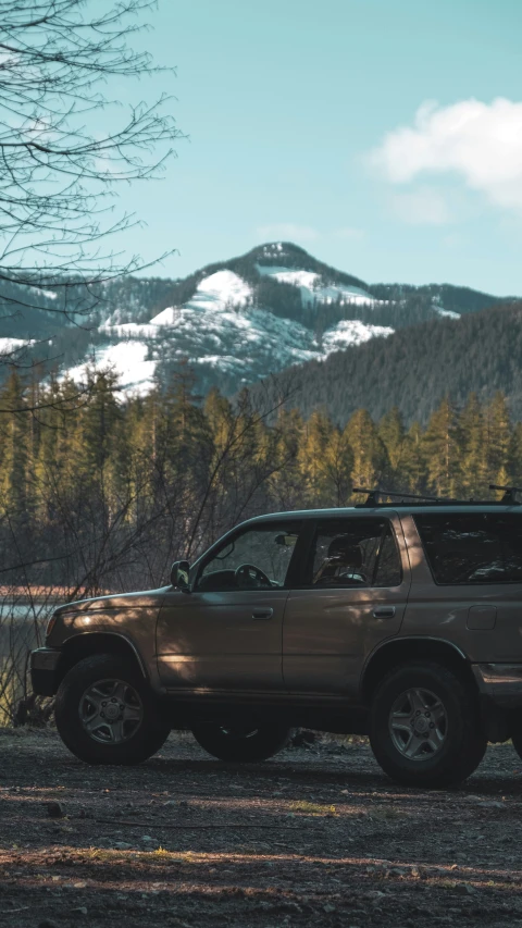 an suv sitting next to water near a snow covered mountain