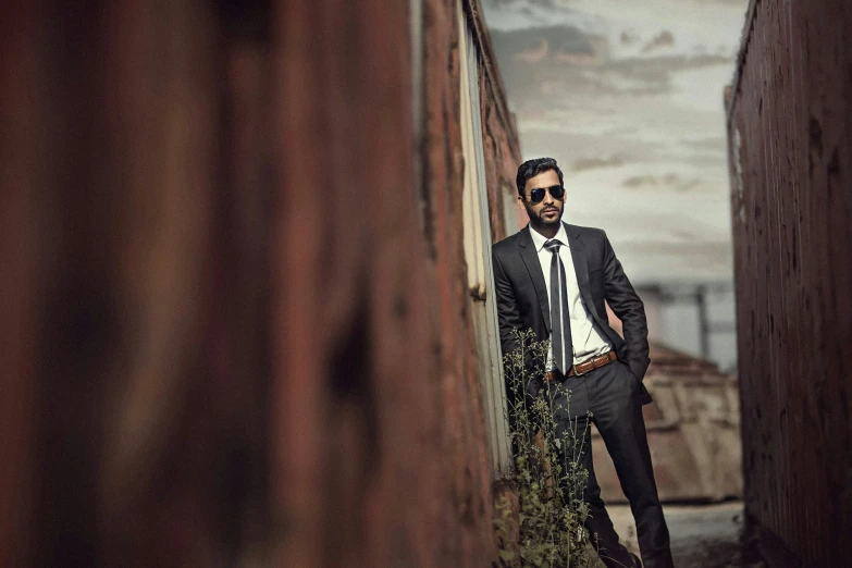 man wearing a suit leaning against the wall with his foot