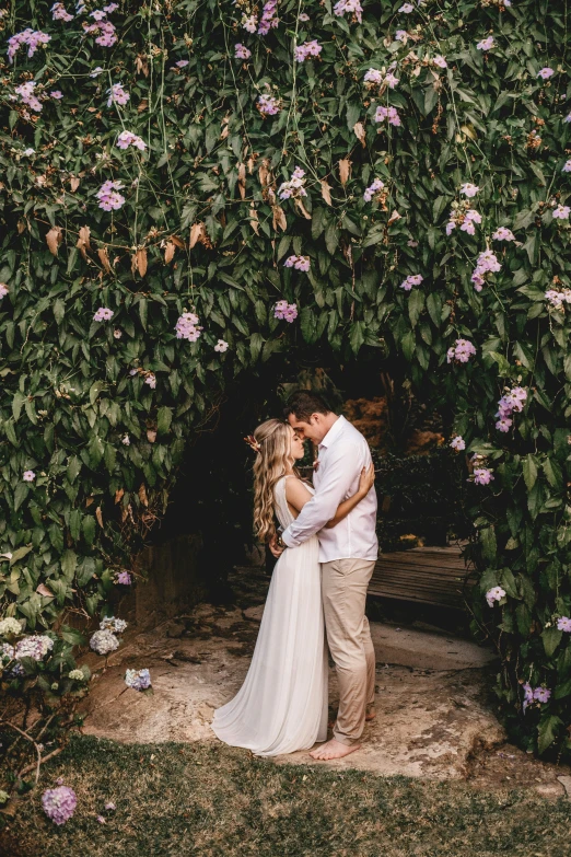 a couple kissing in front of a wall full of flowers