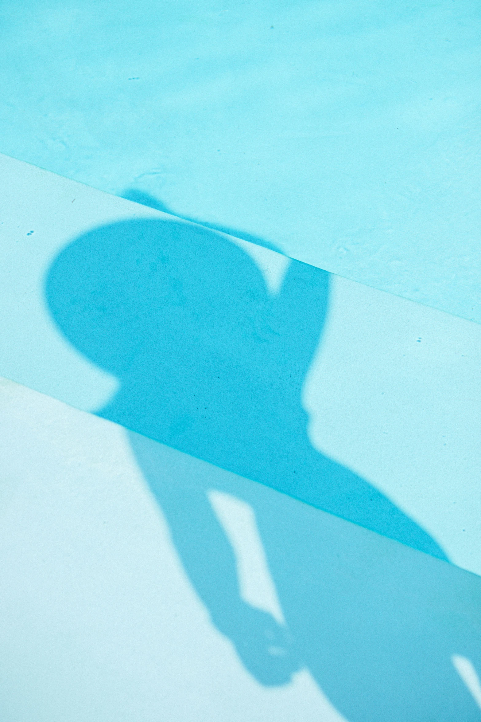 the shadow of someone standing on a sidewalk holding a skateboard