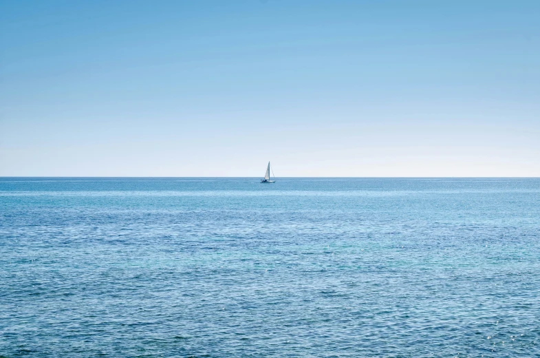 the blue ocean is clean and calm with a sailboat in the distance