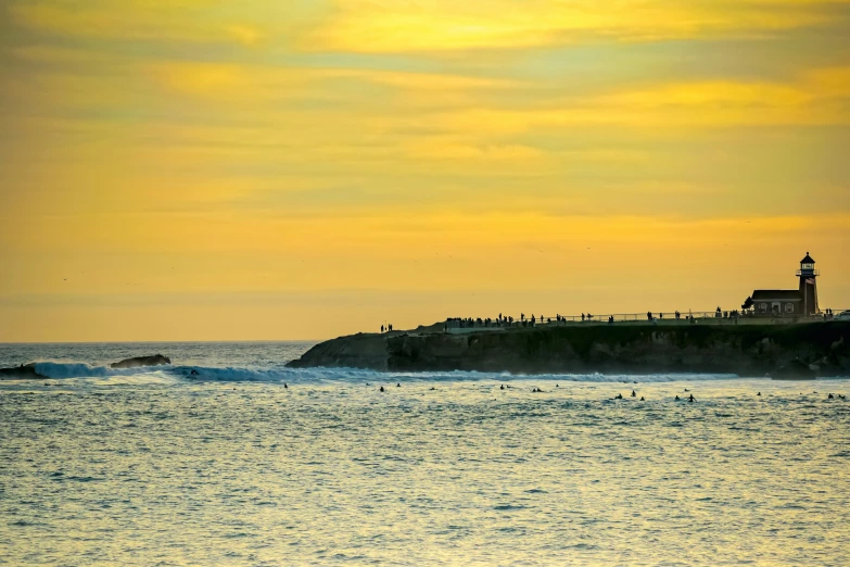 a sunset view of the ocean and a large light house on top of a hill