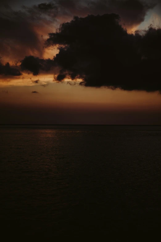 a lone plane flying through a cloudy sky over the ocean