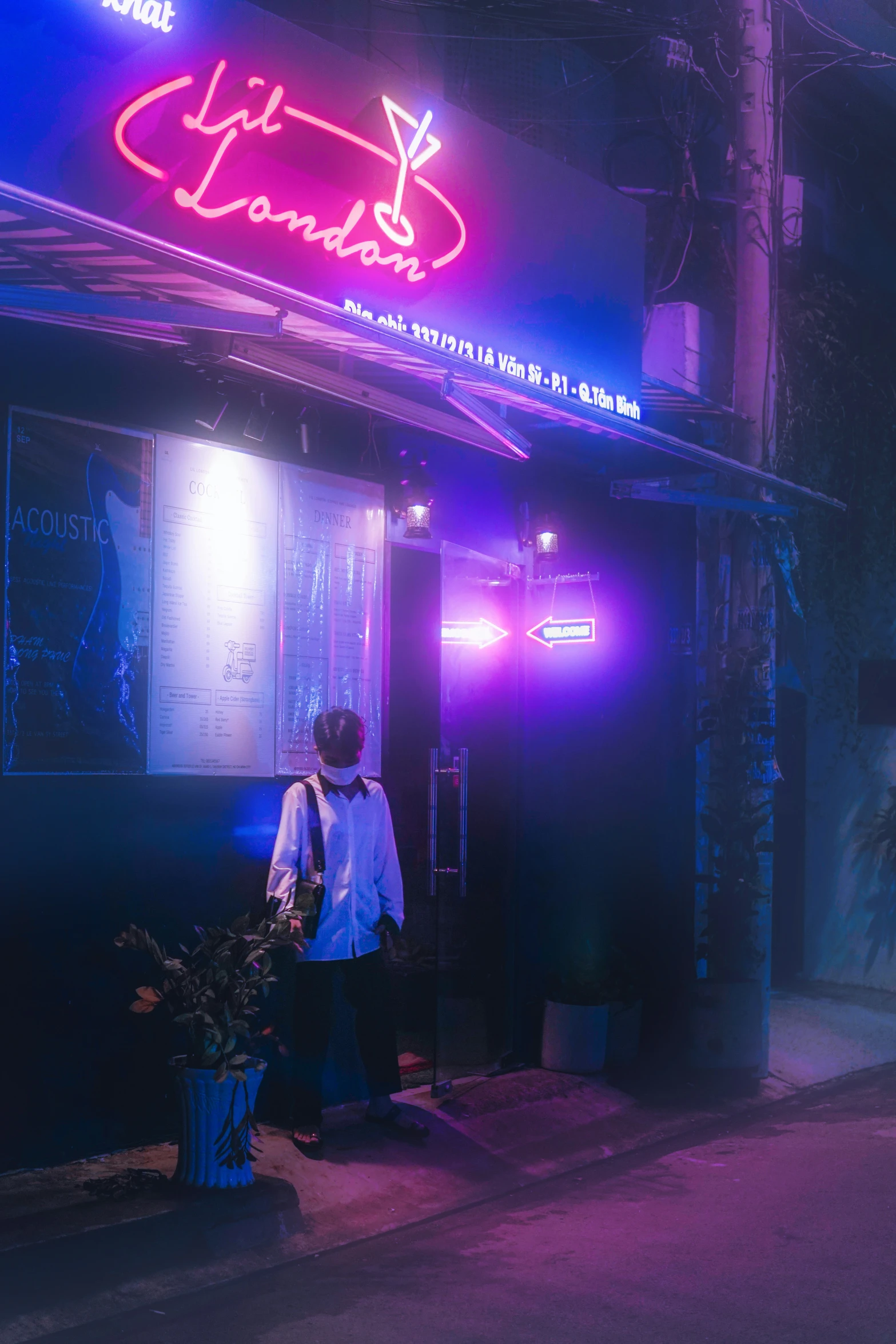 a person stands at a corner of a street in front of an empty building with lights on the front and side of it