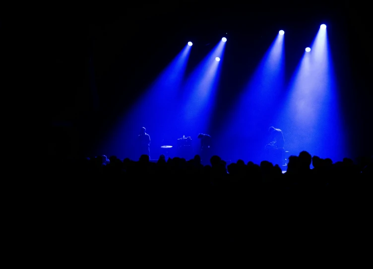 three blue lights illuminate a band at a concert