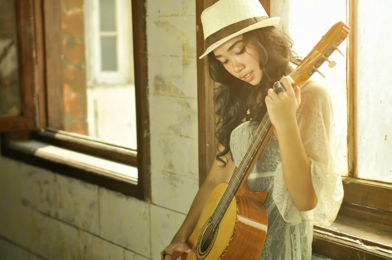 a young woman holding a guitar and looking at her hat