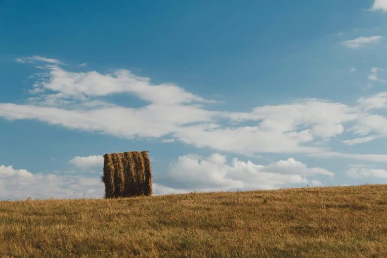 hay stack at the top of a hill under a cloud filled blue sky