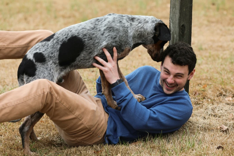 man in blue sweater hugging a spotted dog