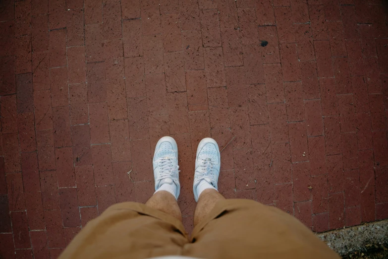 person wearing brown pants and white shoes with white shoes on, facing the camera, sitting outside