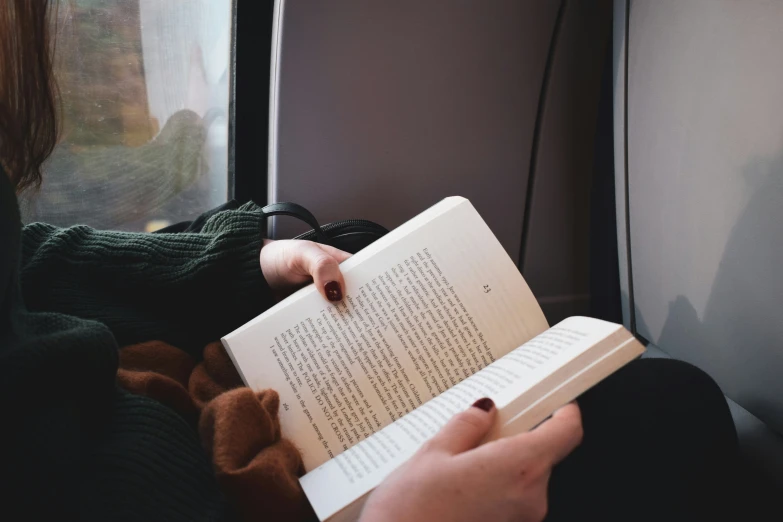 someone's hands reading a book on the train