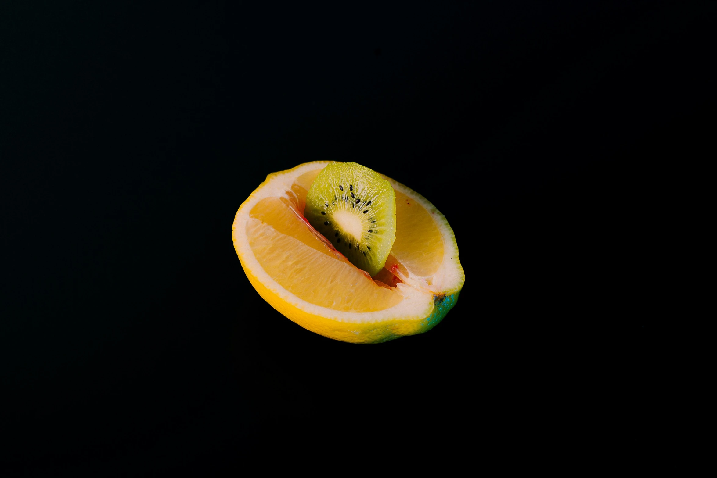 sliced fruit, half with stem and green, on black background