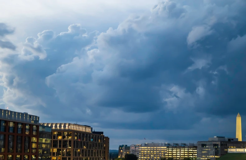 the clouds loom over the skyline of an illuminated city