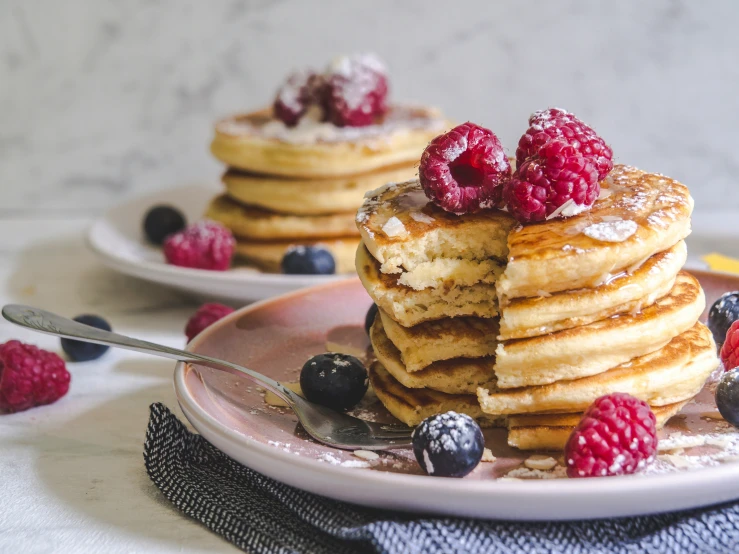 two white plates topped with pancakes and berries