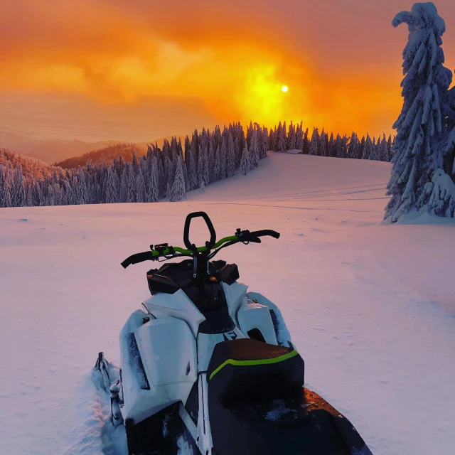 a snowmobile on top of a snowy mountain with the sun setting in the distance