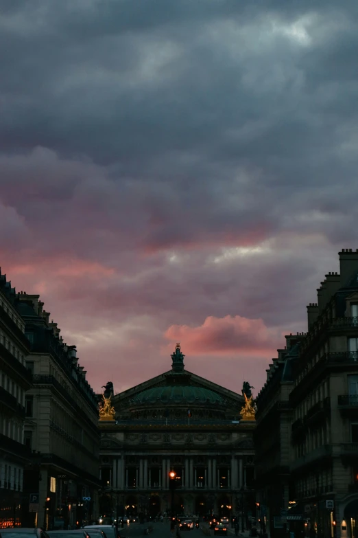 city buildings in the dark with clouds and lights shining at them