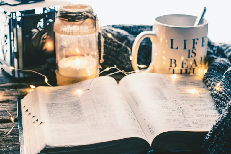 an open book on top of a wooden table next to a lit candle and jar of candles