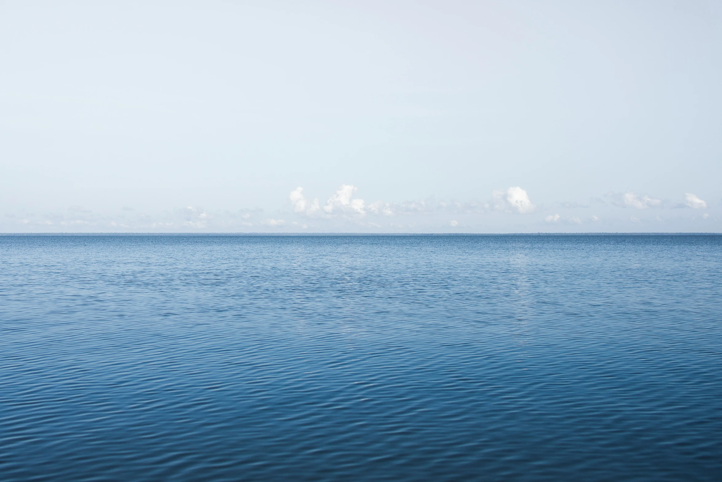 the ocean with some clouds and a boat in the distance