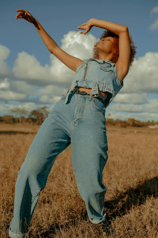 the young person in blue jeans jumps and poses with her arms up